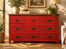 Load image into Gallery viewer, Commode 9 tiroirs peinte en rouge patiné, dans un salon avec plantes et lampe